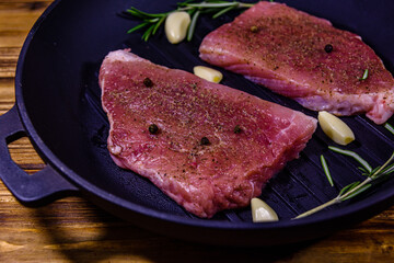 Raw steaks with garlic, rosemary and spices in a cast iron grill pan