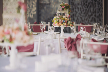 Wedding decoration with pink flowers in vases. The table for guests, served with cutlery, flowers and crockery and covered with a tablecloth. Elegant tablescape.