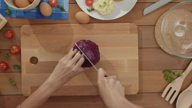 Hand of young Asian woman chef hold knife cutting Red cabbage on wooden board on kitchen table in house. Cooking vegetable salad, Lifestyle healthy food and traditional natural concept. Top view shot.