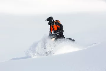 Fotobehang A man in protective equipment on a snowmobile rides along the snowy slopes. © kazantsevaov