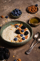 Oatmeal porridge with nuts, fresh berries and honey in a ceramic bowl on rustic background