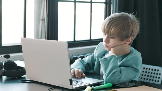 Sad and bored young teenager boy kid using laptop for study online. Exhausted little businessman working on computer. Younger z gen and modern tech easy comfort usage. Kid doing homework feels tired 