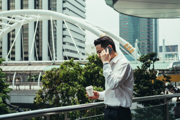 Businessman in office suit talking on mobile phone at balcony outdoors.
Serious businessman talking on phone while standing on office balcony with cup of coffee. Copy space on left