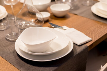 Table with plates and glasses before a party.Piles of white ceramic tableware, plates, saucers, cups on a wooden table. kitchenware.Festive table