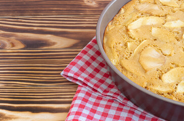 freshly made apple pie in a baking dish. Stands on a red-white napkin in a cage on a black, wooden background. Homemade baking concept. High quality photo