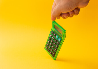 calculator held with a finger with yellow background, mathematics, cost, tax or investment...