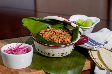 Delicious traditional Mexican dish of pork, cochinita pibil, on a wooden board, lemon and purple onion. Mexican food, Yucatan, Mérida.