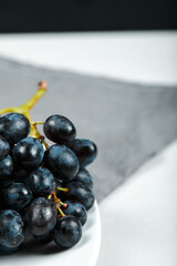 Black grape on white plate with grey tablecloth