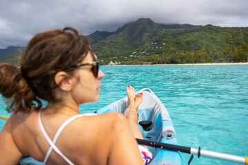 Woman rests on a kayak floating above turquoise colored tropical ocean water near island of Moorea