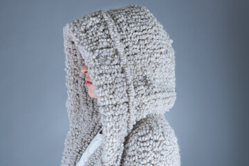 A woman in a beige hoodie. Grey background.