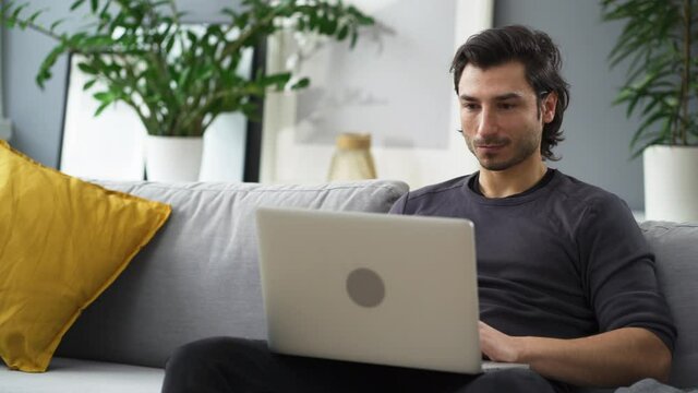 Happy young man working on laptop sitting on the sofa at home