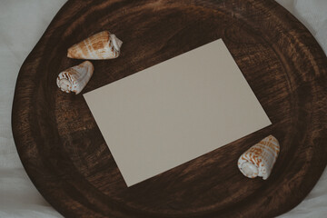 White paper card on wooden tray with seashells in boho style