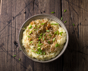 Traditional Irish dish colcannon, mashed potatoes with cabbage and green onions, on top of crispy fried cabbage topping with nuts and spices on a wooden table