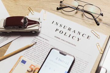 Flat lay of vehicle insurance policy. Magnifier, retro car toy and cash