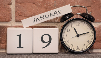 Important date, January 19, winter season. Calendar made of wood on a background of a brick wall. Retro alarm clock as a time management concept.