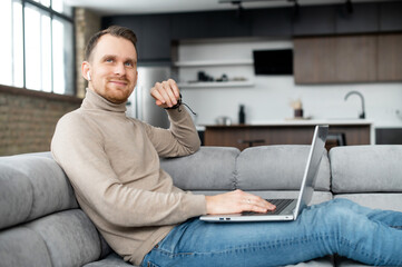 Inspired programmer with earphones and laptop on the lap, smiling looking up, sitting on a sofa,...