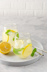 Traditional lemonade with lemon, mint and ice in a glass with metal straw on a gray concrete background. Refreshment summer drink. Copy space.