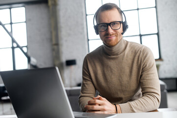 Confident operator with headset and glasses, looking at the camera, sitting at the laptop, worker...