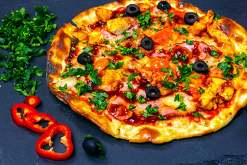 Pizza with ham and chicken on slate board.