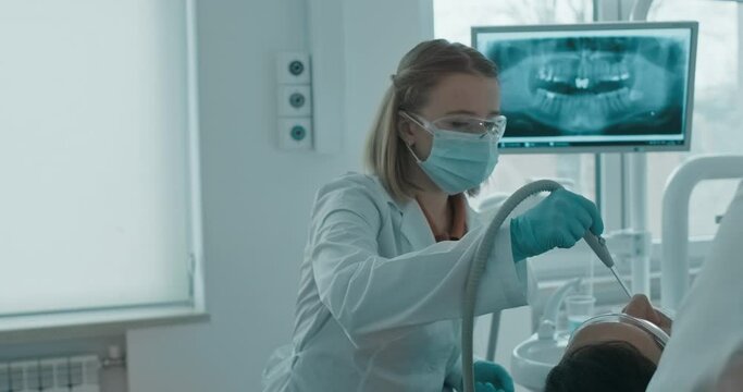 A female nurse at the dentist`s office is helping the dentist with the dental procedures and holding a saliva ejector inside the patient&rsquo;s mouth.
