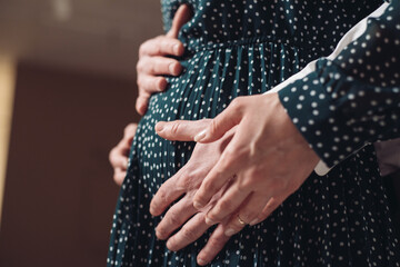 A pregnant woman holds her husband's hands on her belly
