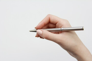 The elegant hand of a girl holding a silver metal pen on a light gray background. A copy of the...