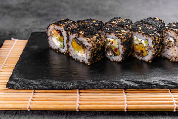 Sushi roll with salmon, avocado and cheese on a black stone plate on a white plate. Sushi menu. Japanese food. black rice sushi