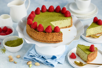 Cheesecake with pistachios and matcha tea decorated with fresh raspberries. Pieces of cheesecake on plates