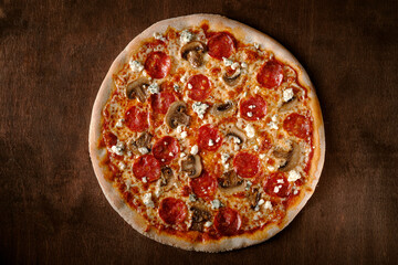 Spicy pepperoni pizza with sausage, mushrooms and goat cheese. Cooked pizza on a wooden table, top view