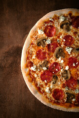 Spicy half pepperoni pizza with sausage, mushrooms and goat cheese. Cooked pizza on a wooden table, top view