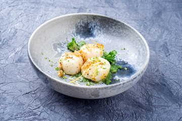 Modern style fried scallops with crumbles and lemon slices served with kalette cilanto relish as close-up on a Nordic design plate with copy space