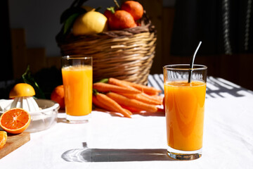 Glass of fresh squeezed orange juice on the table of the kitchen. Ripe bio citrus fuits and vegetables in background.