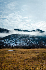 Wintery landscape with clouds and sun, yellow field, snow on a hill