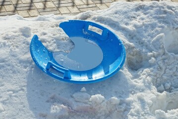 one broken round blue plastic sled plate lies on a snowdrift of white snow outside