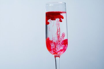 Red tattoo pigment dissolved in a glass of water. Hand stirring pigment in water