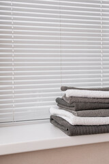Obraz na płótnie Canvas Neatly folded bath cloth in grey and white colors above white window blind.