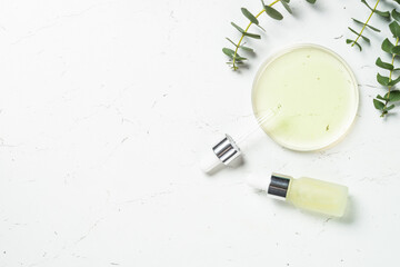 Essential oil, eucalyptus oil with green leaves. Glass petri dish with essential oil at white background.