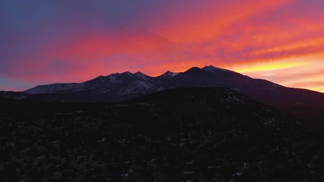 A crimson red sunset behind the San Francisco Peaks and Humphreys Peak, north of Flagstaff, Arizona. An aerial shot trucking right to left.