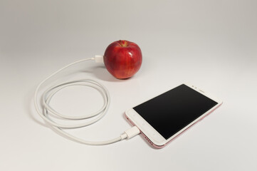 A smartphone connected to an apple with a white USB cable on the neutral gradient background. The green power seems to pass from the fruit to the phone.