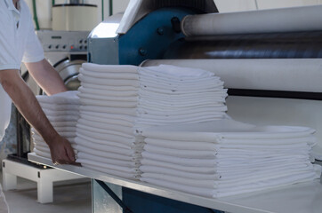 Unrecognizable man stacking freshly ironed sheets or fabrics in an industrial laundry.