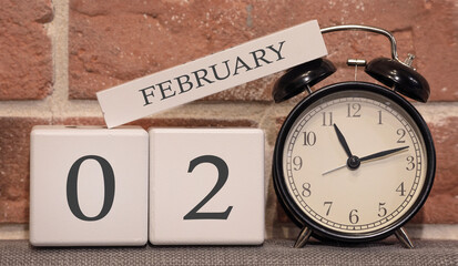 Important date, February 2, winter season. Calendar made of wood on a background of a brick wall. Retro alarm clock as a time management concept.