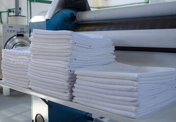 Stack of folded clean sheets or fabrics and industrial iron in an industrial laundry.