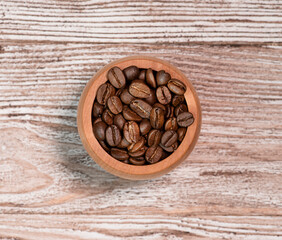 Coffee beans in a wooden glass on a wooden background.