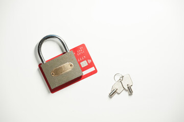 A gray metal padlock with a pair of keys and red credit card on the white background. Top view