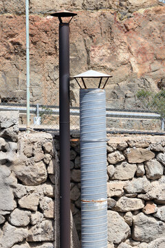 Two Tubular Steel Industrial Chimneys against Rough Stone Wall & Wire Fence
