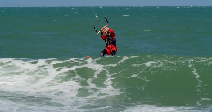Athlete showing sport trick jumping with kite and board in air. Extreme water sport and summer vacations concept. Acrobatic jump of professional kite surfer on the sea wave.