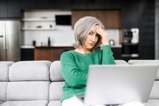 Upset senior woman looks at the laptop screen and feels frustrated, win in lottery, has a problem with job. A mature retired lady receive a bad news or can not afford bills