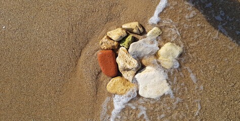 colorful pebbles on the beach in yellow sand and sea foam