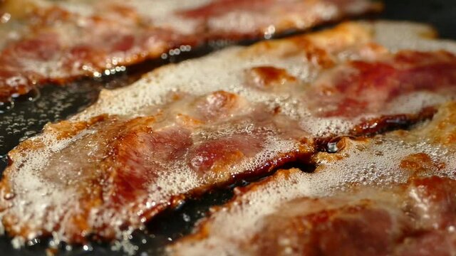 Fry the bacon in a pan. A slice of pork bacon is prepared in its own fat. Layer of meat and lard. Close up in the kitchen.
