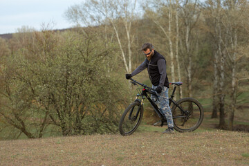 Naklejka premium Sports brutal bearded guy on a modern mountain bike. Cyclist on the green hills in the spring.